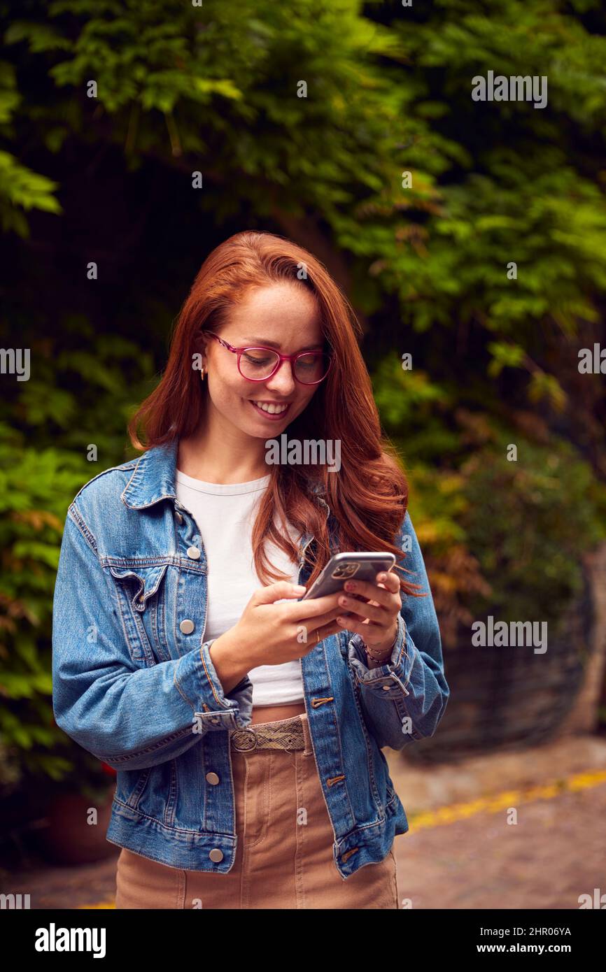 Vlogger femminile o Social Influencer in città utilizzando il telefono cellulare sulla strada per la posta ai social media Foto Stock