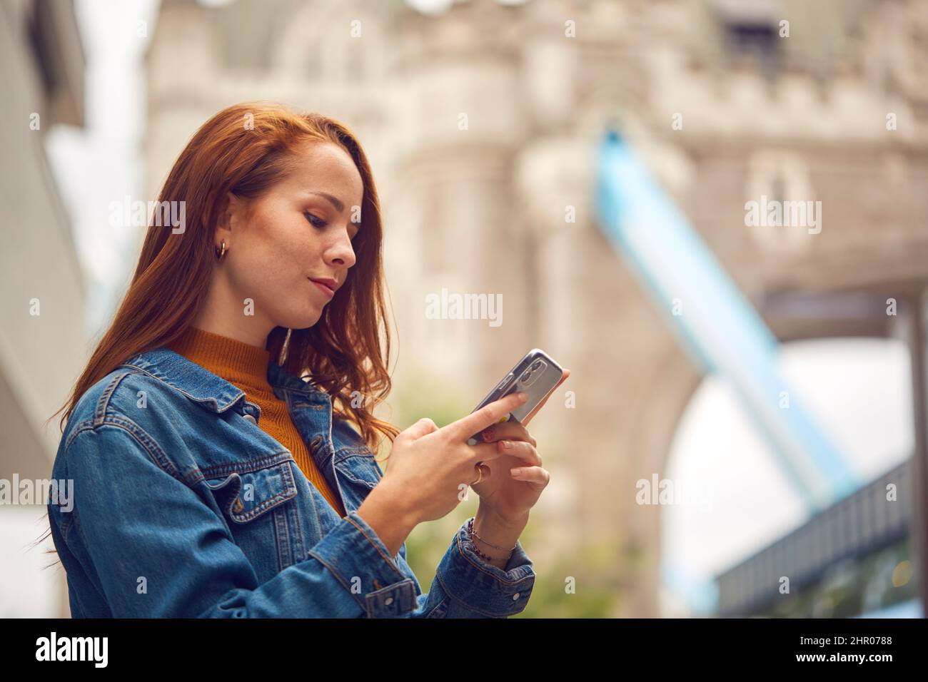 Vlogger femminile o Social Influencer viaggiando attraverso Londra usando il cellulare vicino al Tower Bridge Foto Stock