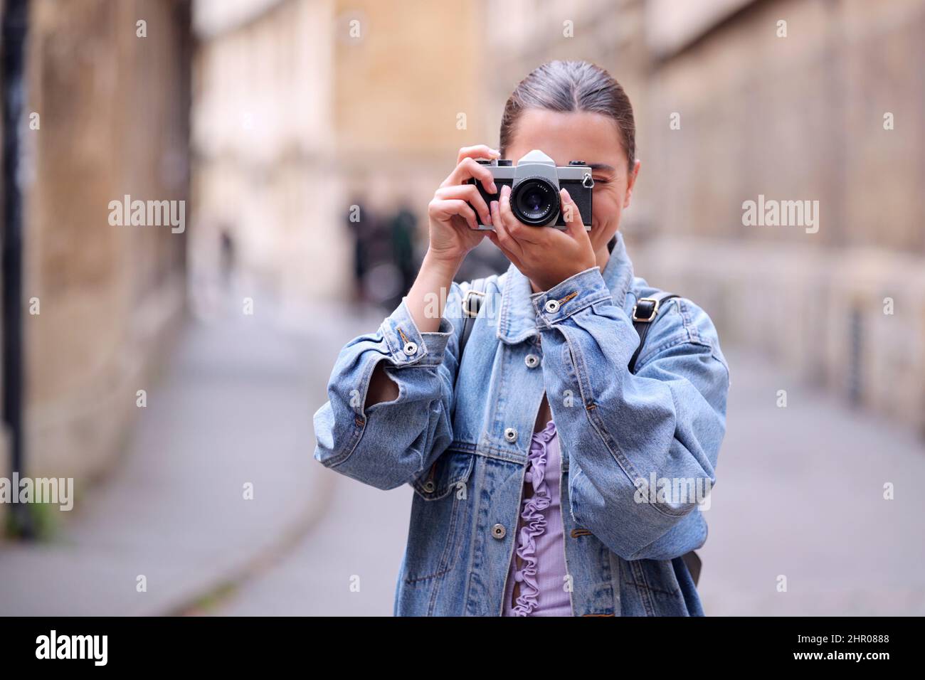 Giovane donna in City Street scattare foto verso la fotocamera su fotocamera digitale stile retro Foto Stock