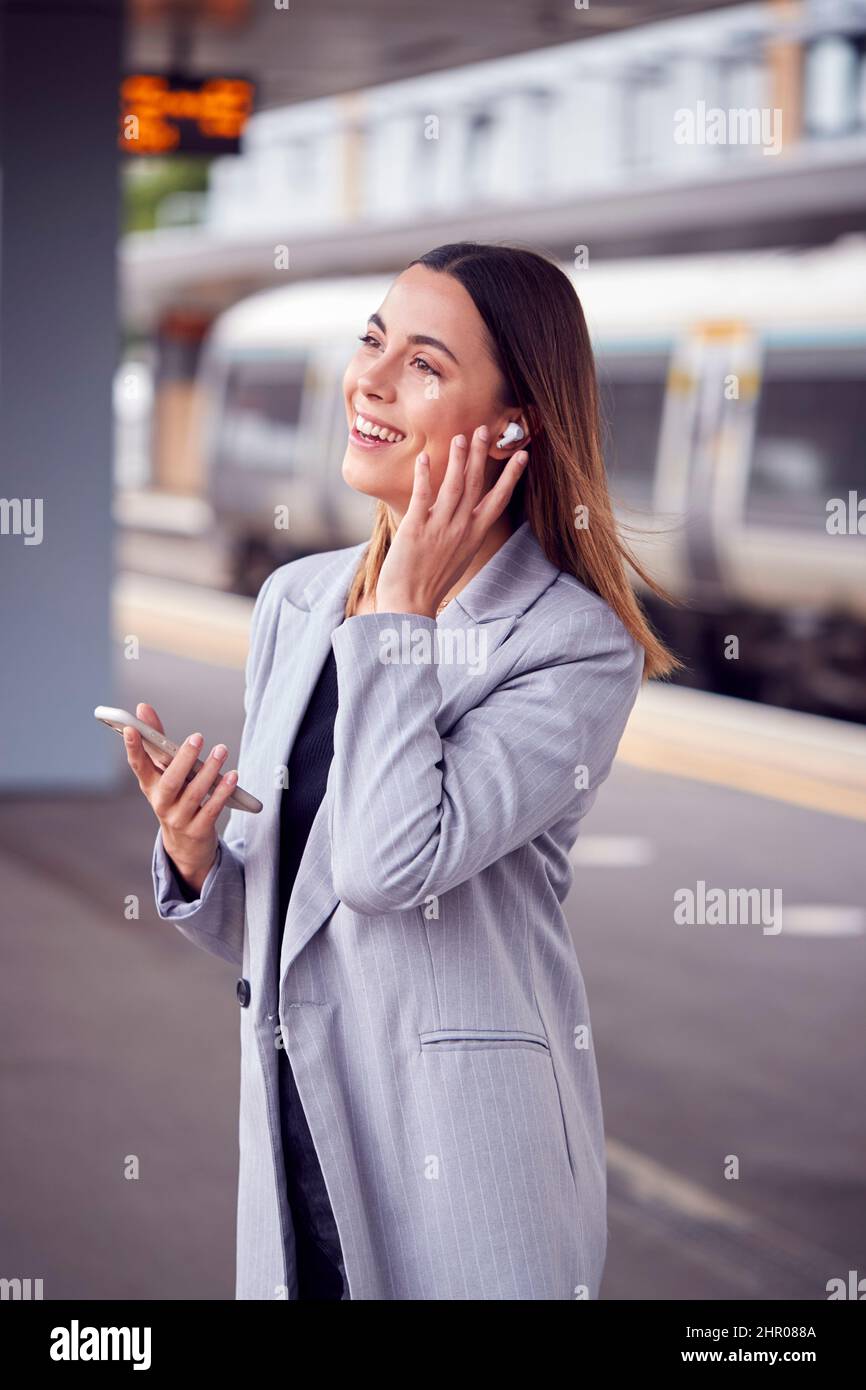 Donna d'affari in attesa sulla piattaforma ferroviaria con auricolari wireless risposte chiamata sul telefono cellulare Foto Stock