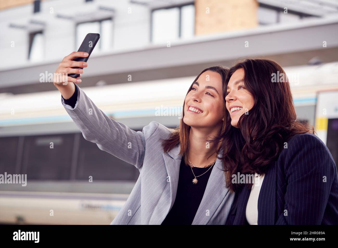 Donne d'affari che viaggiano per lavoro in attesa di treno sulla piattaforma della stazione prendendo Selfie su cellulare Foto Stock