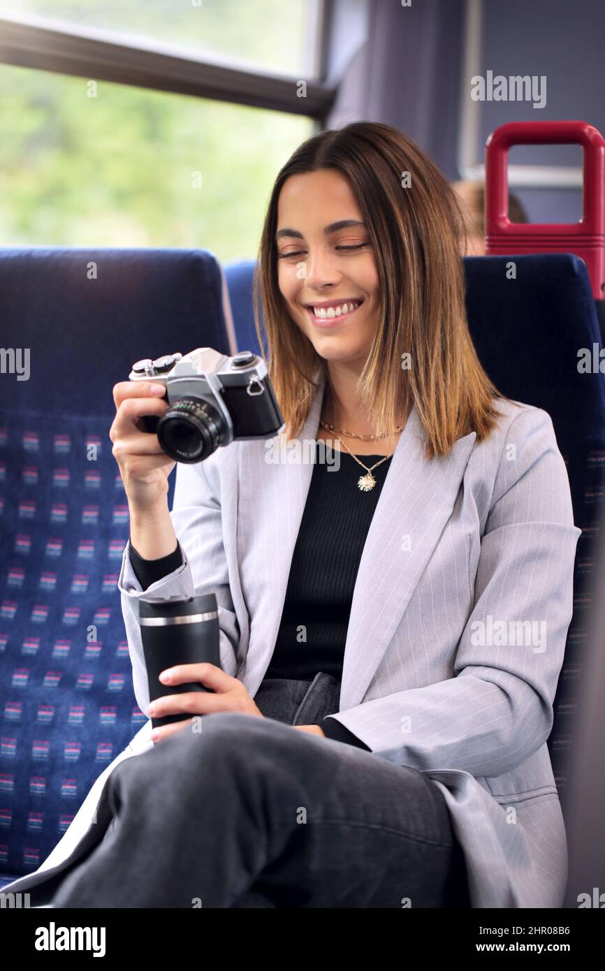 Sorridente Businesswoman in viaggio per lavorare in treno guardando le foto sulla fotocamera digitale retrò Foto Stock