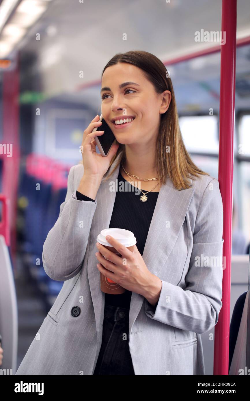 Donna in piedi Businesswoman con il caffè Takeaway che fa il pendolarismo per lavorare sul treno che parla sul telefono cellulare Foto Stock
