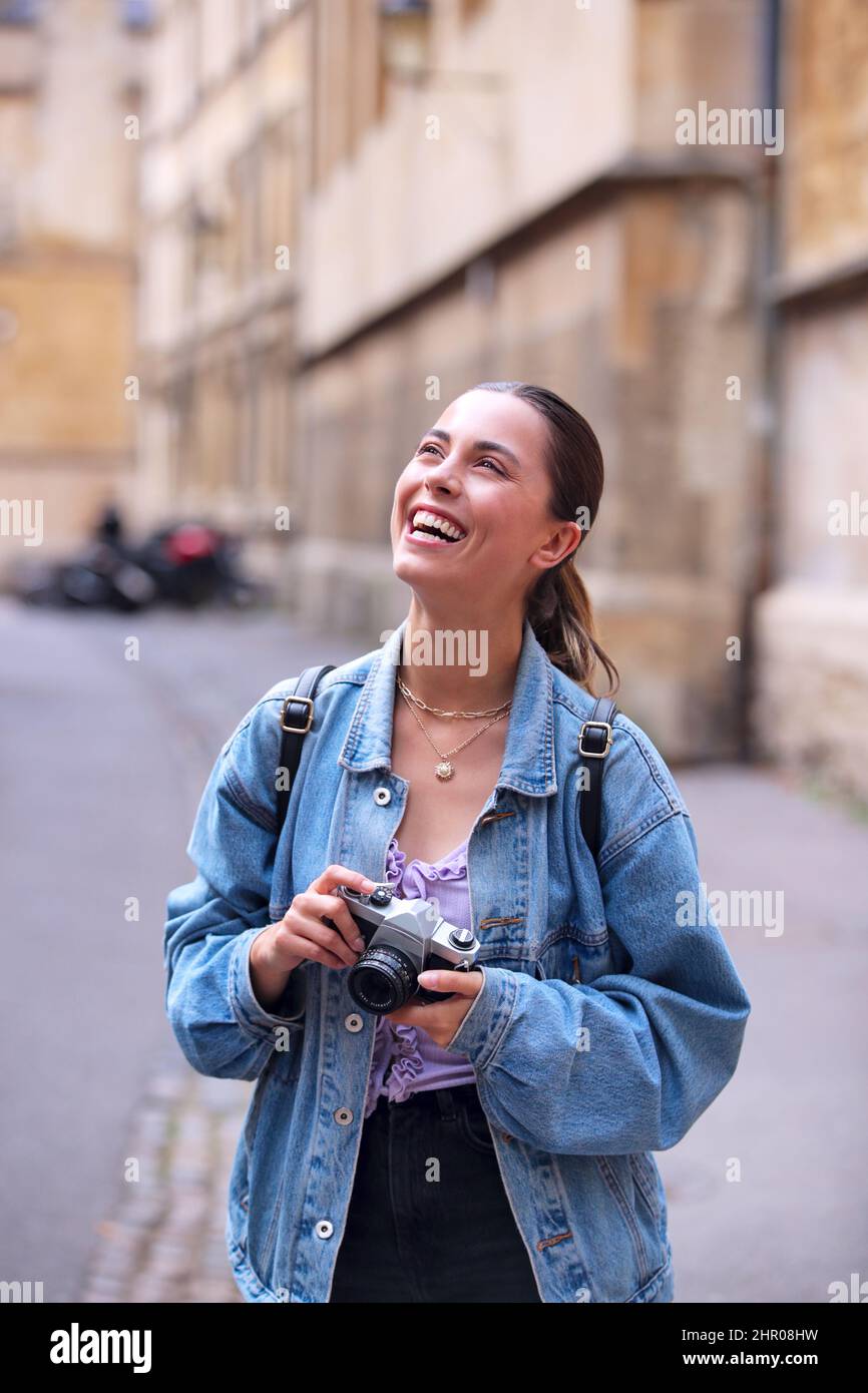 Giovane donna in City Street scattando foto sulla macchina fotografica digitale di stile retro per pubblicare sui social media Foto Stock