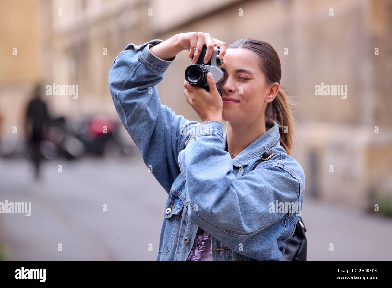 Giovane donna in City Street scattando foto sulla macchina fotografica digitale di stile retro per pubblicare sui social media Foto Stock