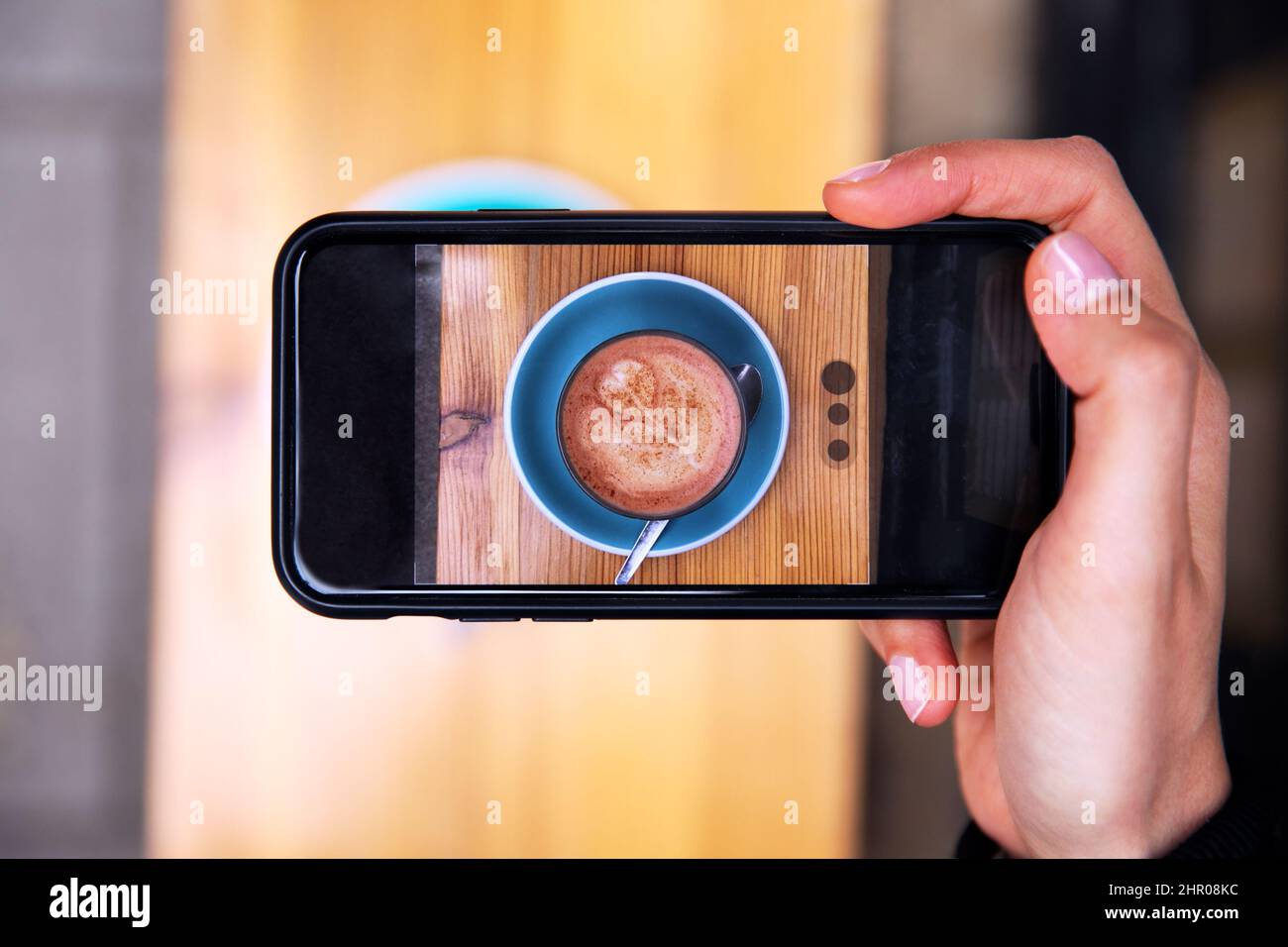 Primo piano della persona che fotografi una tazza di caffè sul telefono cellulare al bar all'aperto o al bar Foto Stock