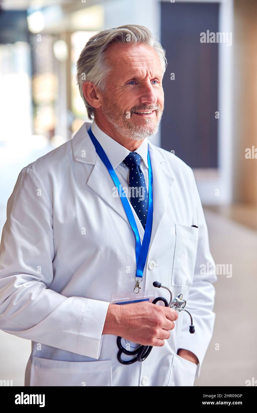 Ritratto del medico maturo sorridente che indossa cappotto bianco in piedi all'interno dell'edificio dell'ospedale Foto Stock
