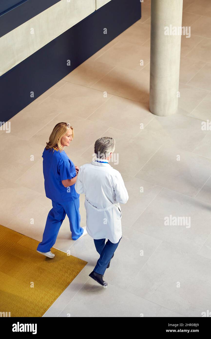 Colpo di testa di medici maschili e femminili in camici e scrub bianchi che camminano attraverso l'ospedale occupato Foto Stock