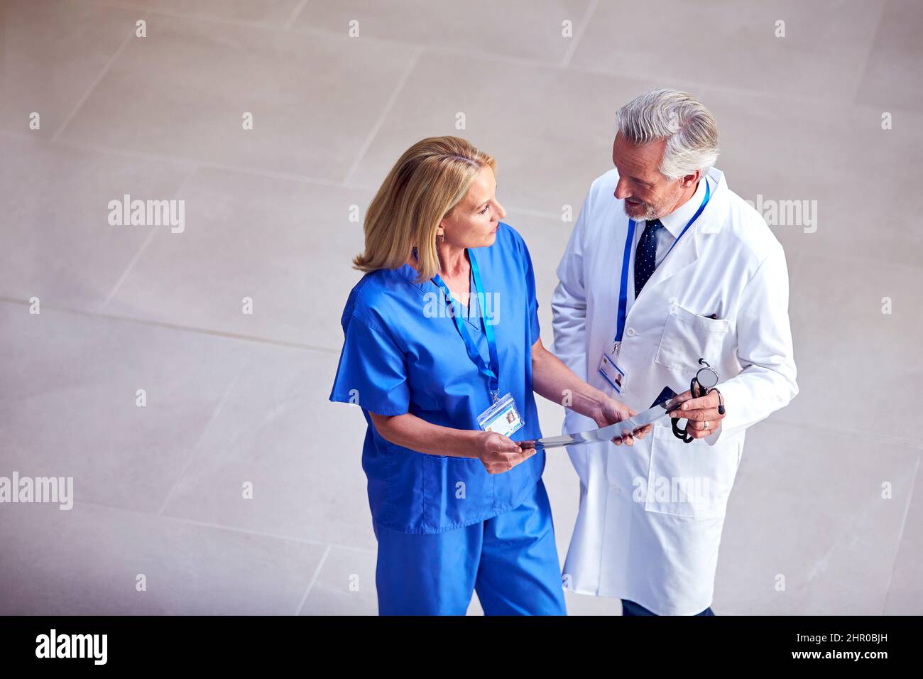 Foto in alto di medico maschile indossando cappotto bianco discutere scansione con collega femminile in scrub Foto Stock