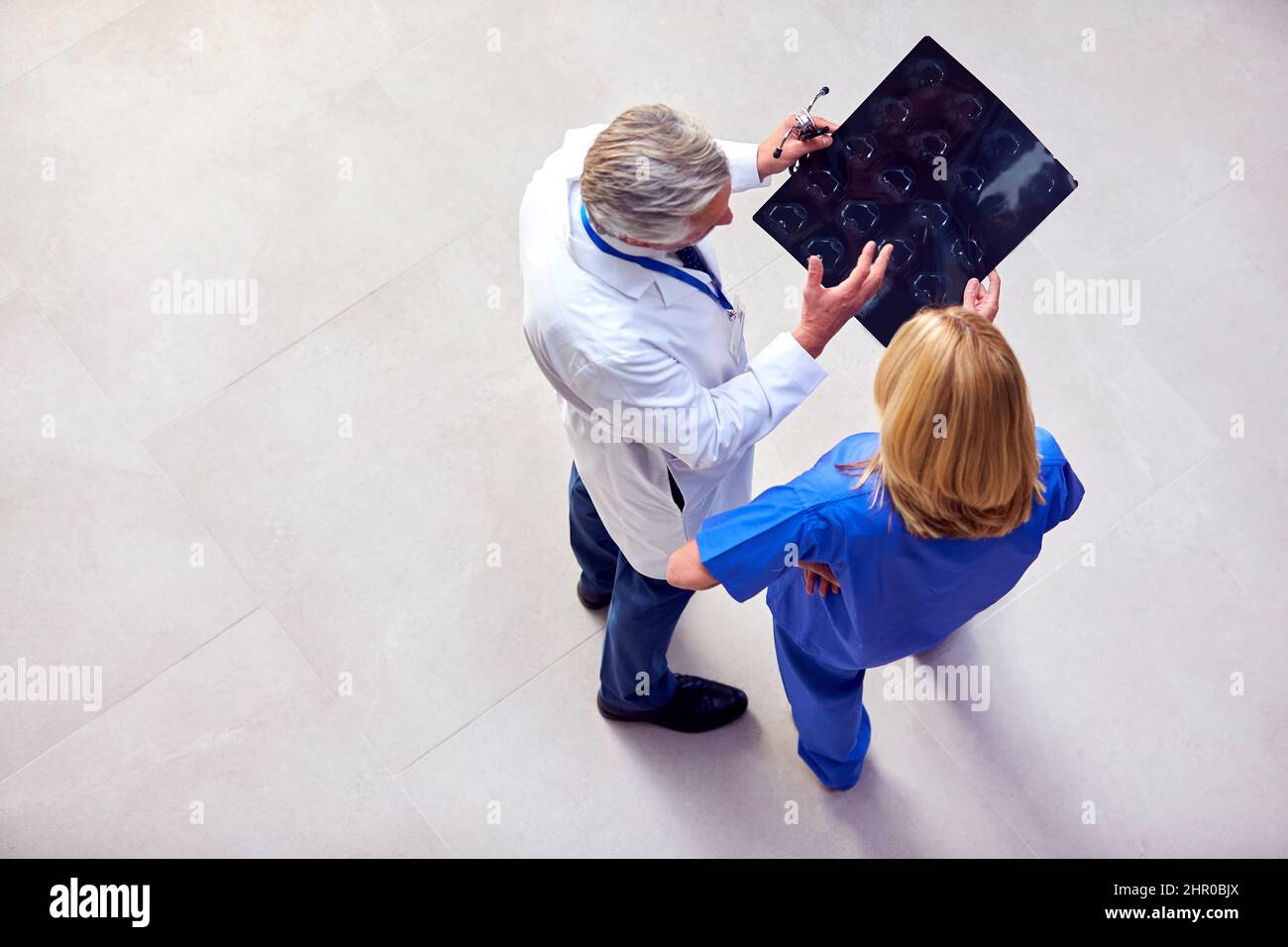 Foto in alto di medico maschile indossando cappotto bianco discutere scansione con collega femminile in scrub Foto Stock