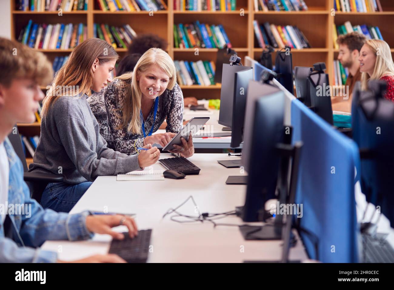 Università femminile o studente universitario che lavora al computer in biblioteca essendo aiutato da Tutor Foto Stock