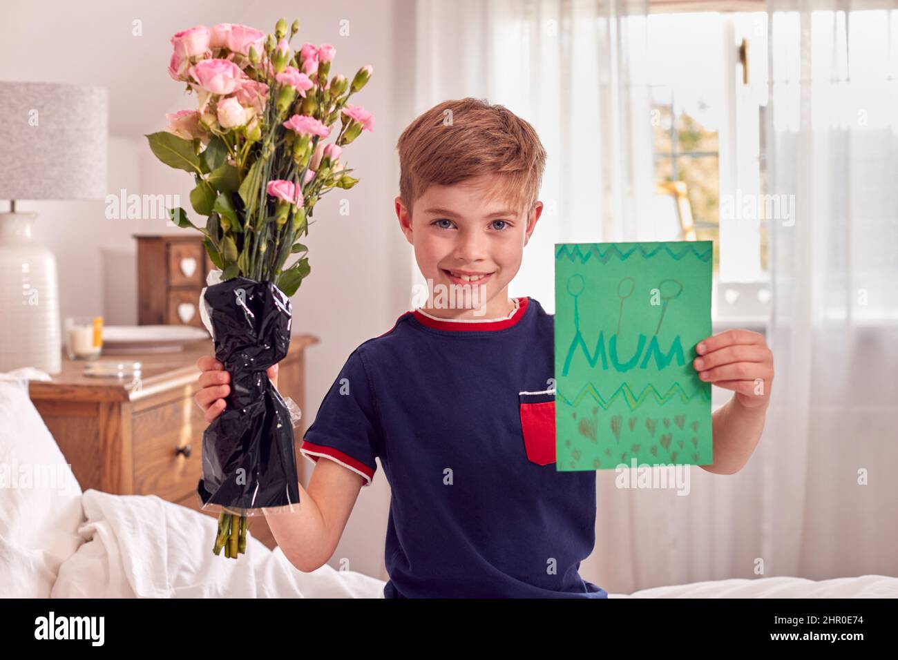 Ritratto di ragazzo a Pajamas con fiori e carta fatta in casa per compleanno o Festa della mamma Foto Stock
