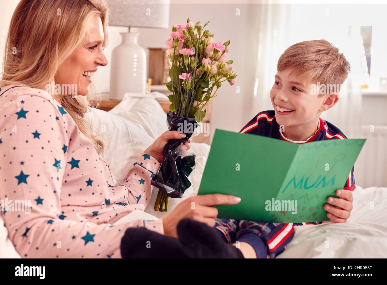 Amorevole Figlio che sorprende la mamma a letto con fiori e carta fatta in casa il compleanno o il giorno della mamma Foto Stock