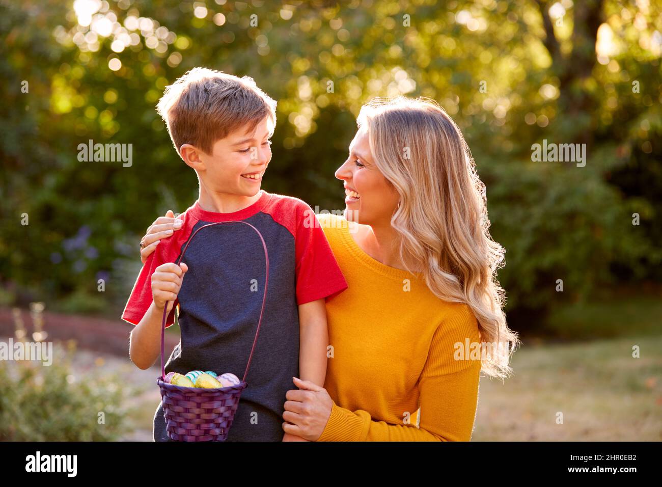 Sorridente madre e figlio a Pasqua Egg Hunt Holding cestello di uova di cioccolato avvolto in un foglio Foto Stock