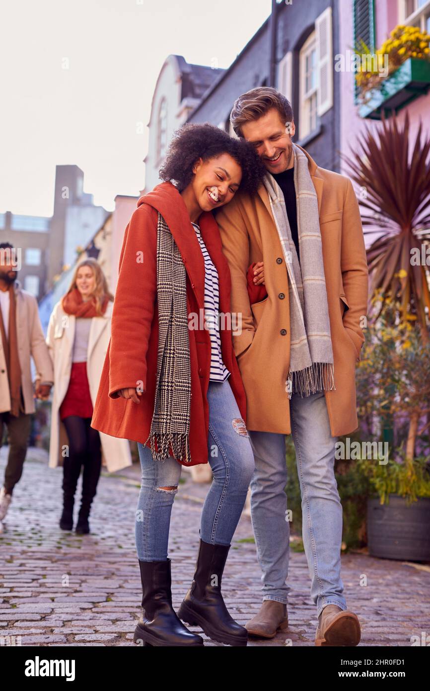 Coppia multiculturale con amici camminando lungo la strada residenziale della città in autunno o in inverno Foto Stock