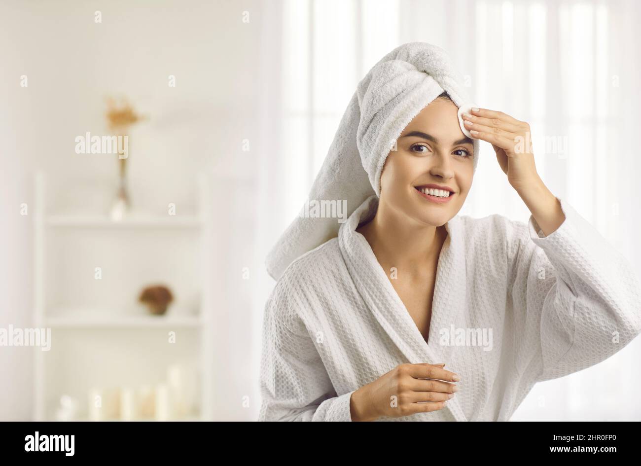 Bella donna al mattino dopo la doccia prima di applicare il trucco pulisce la pelle con cotone tampone. Foto Stock