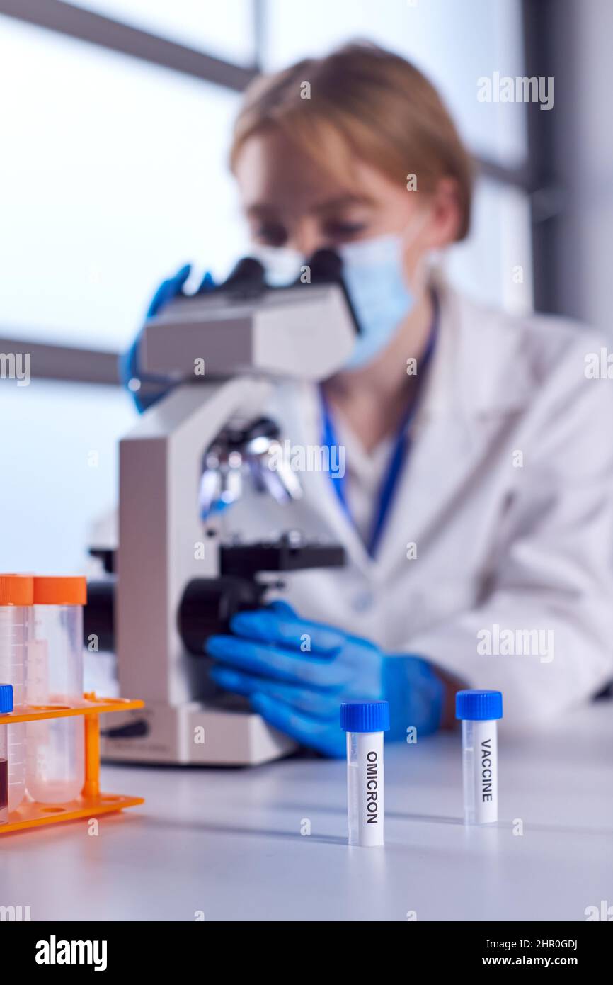 Lavoratore di laboratorio femminile che indossa PPE cercando Covid-19 variante Omicron e vaccino con microscopio Foto Stock