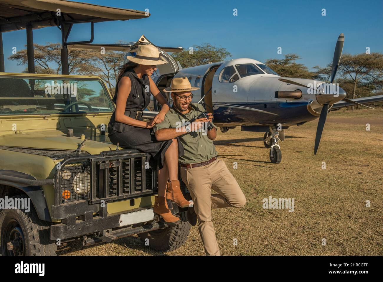 Una giovane e attraente coppia tanzaniana che indossa abiti tropicali, in safari in una riserva di caccia, accanto al loro aereo privato noleggiato. Foto Stock