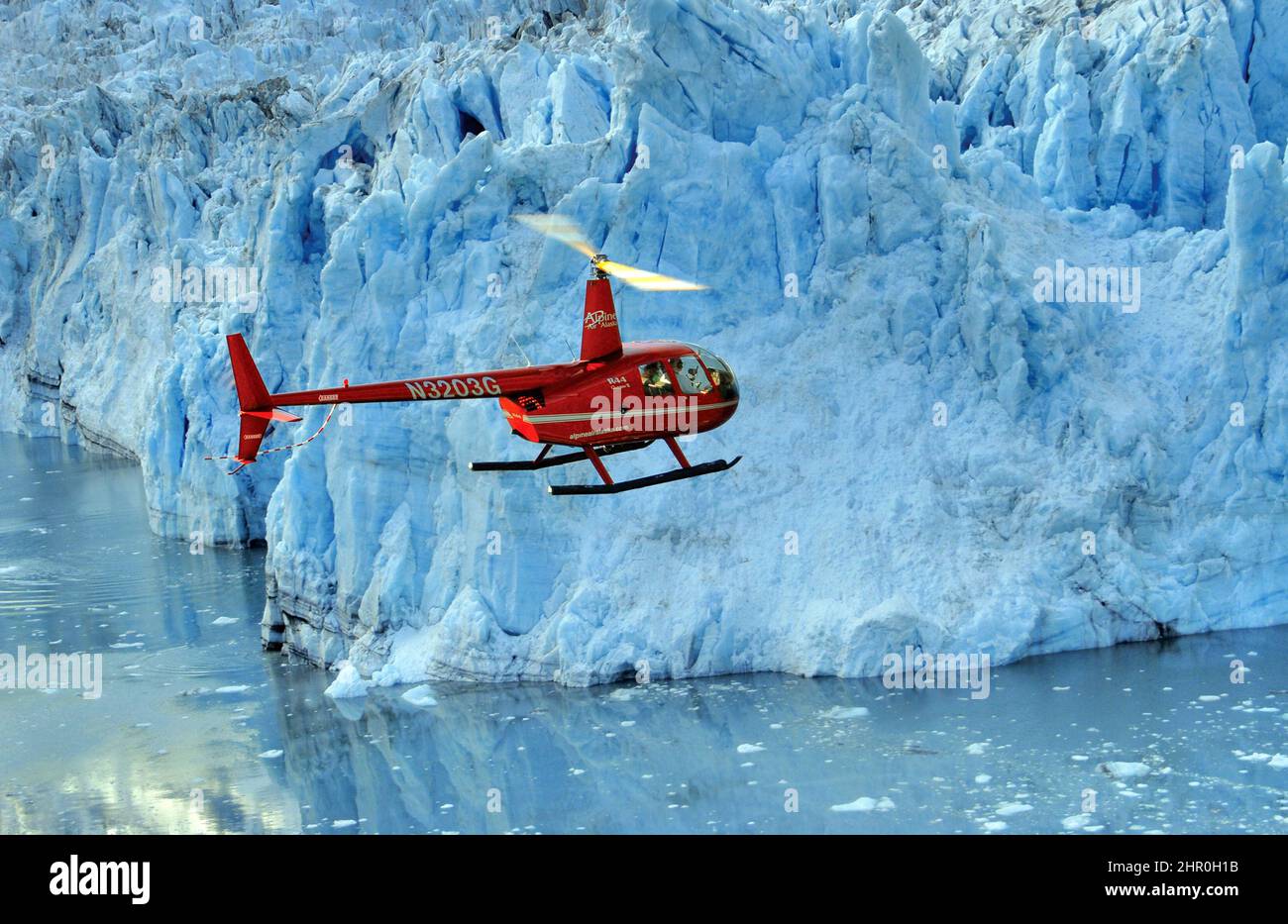 Un elicottero Robinson R44 da Alpine Air Alaska che vola vicino a un ghiacciaio. Foto Stock