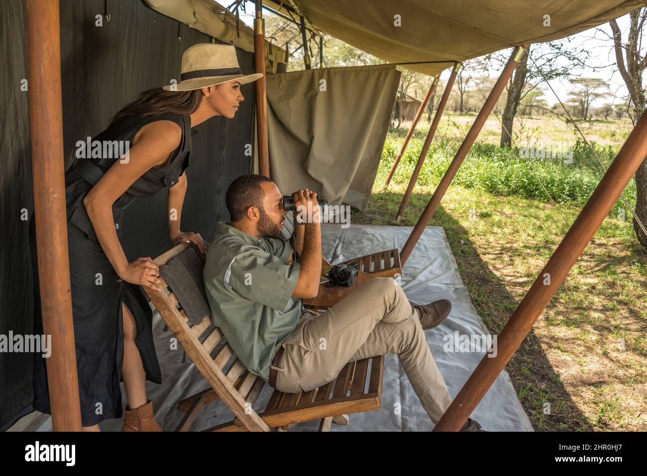 Una giovane e attraente coppia tanzaniana che indossa abiti tropicali, in safari in una riserva di caccia, accanto al loro aereo privato noleggiato. Foto Stock