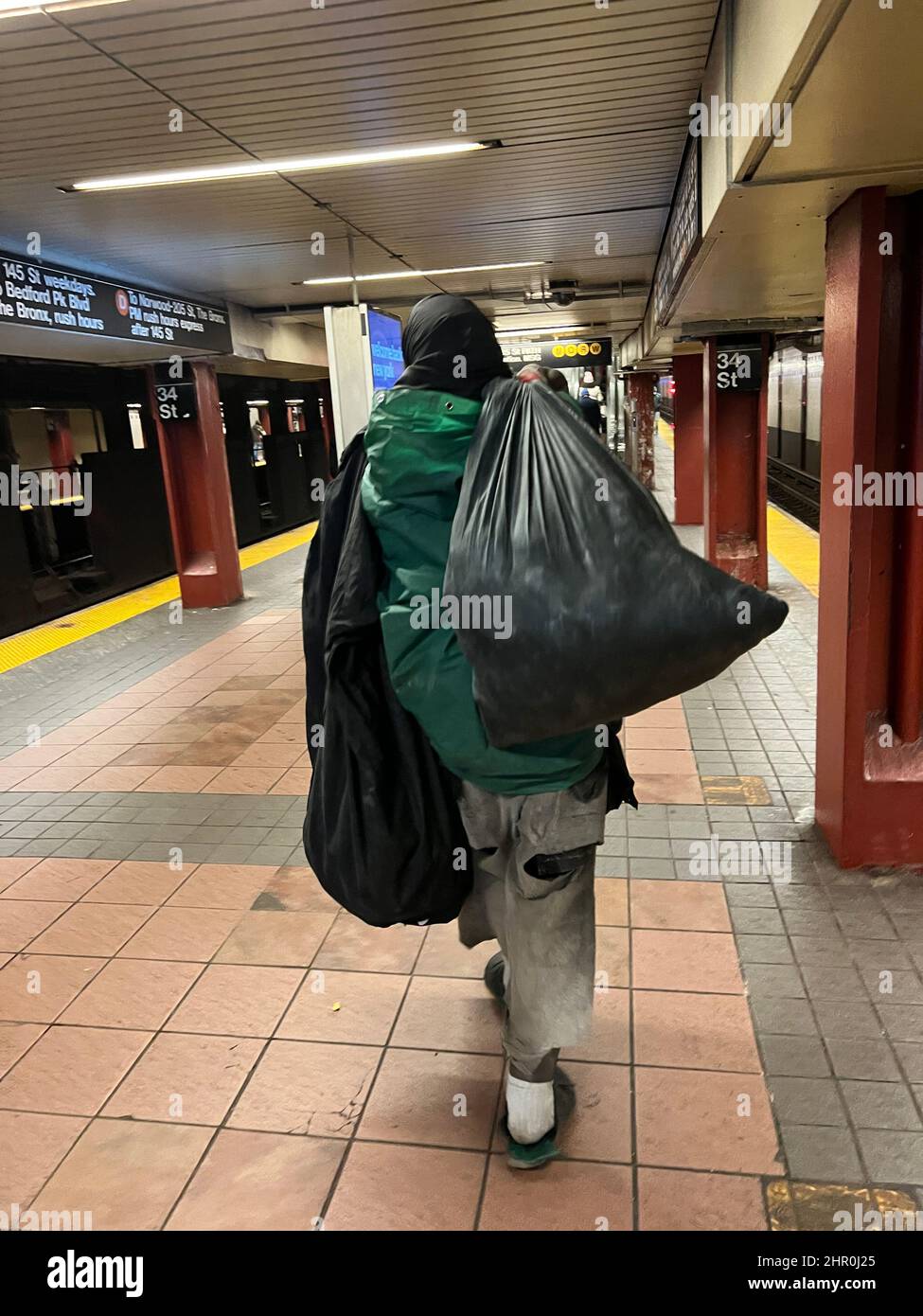 Un uomo senza tetto ragged con sacchi di spazzatura pieni di cose sul binario alla stazione 34th Street Broadway a New York City. Foto Stock