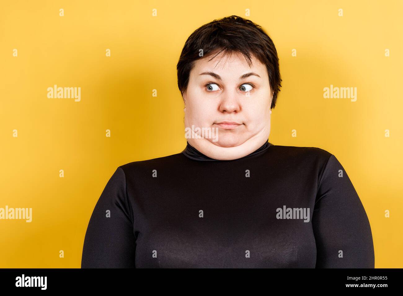 donna grassa con doppio mento e aspetto pazzo su sfondo giallo Foto Stock