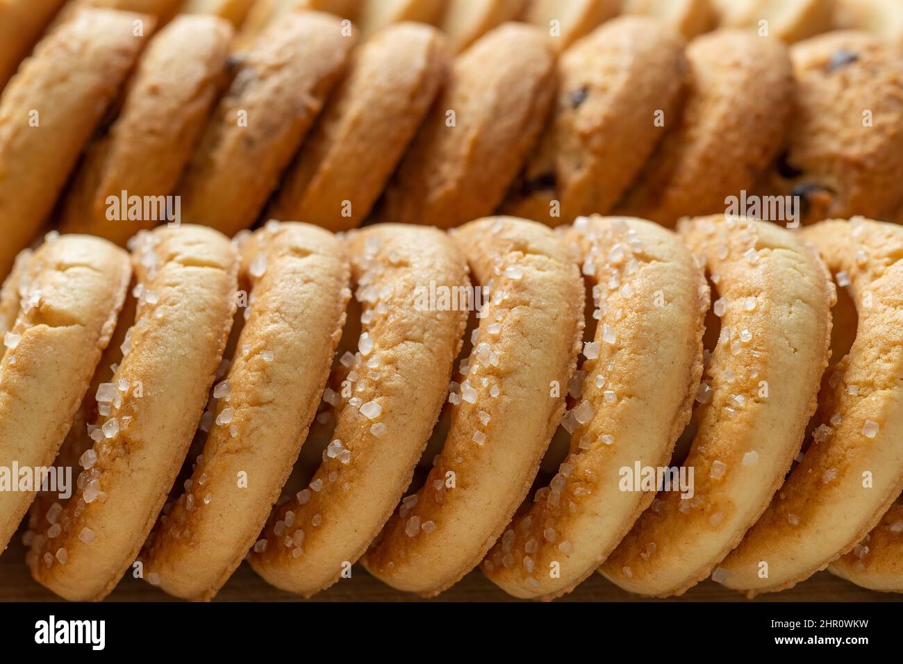 Croccanti biscotti di zucchero frollino fondo macro. Fila di gustosi biscotti al burro con primo piano di zucchero. Texture di pasticceria al forno per colazione. Cibo dolce. Foto Stock
