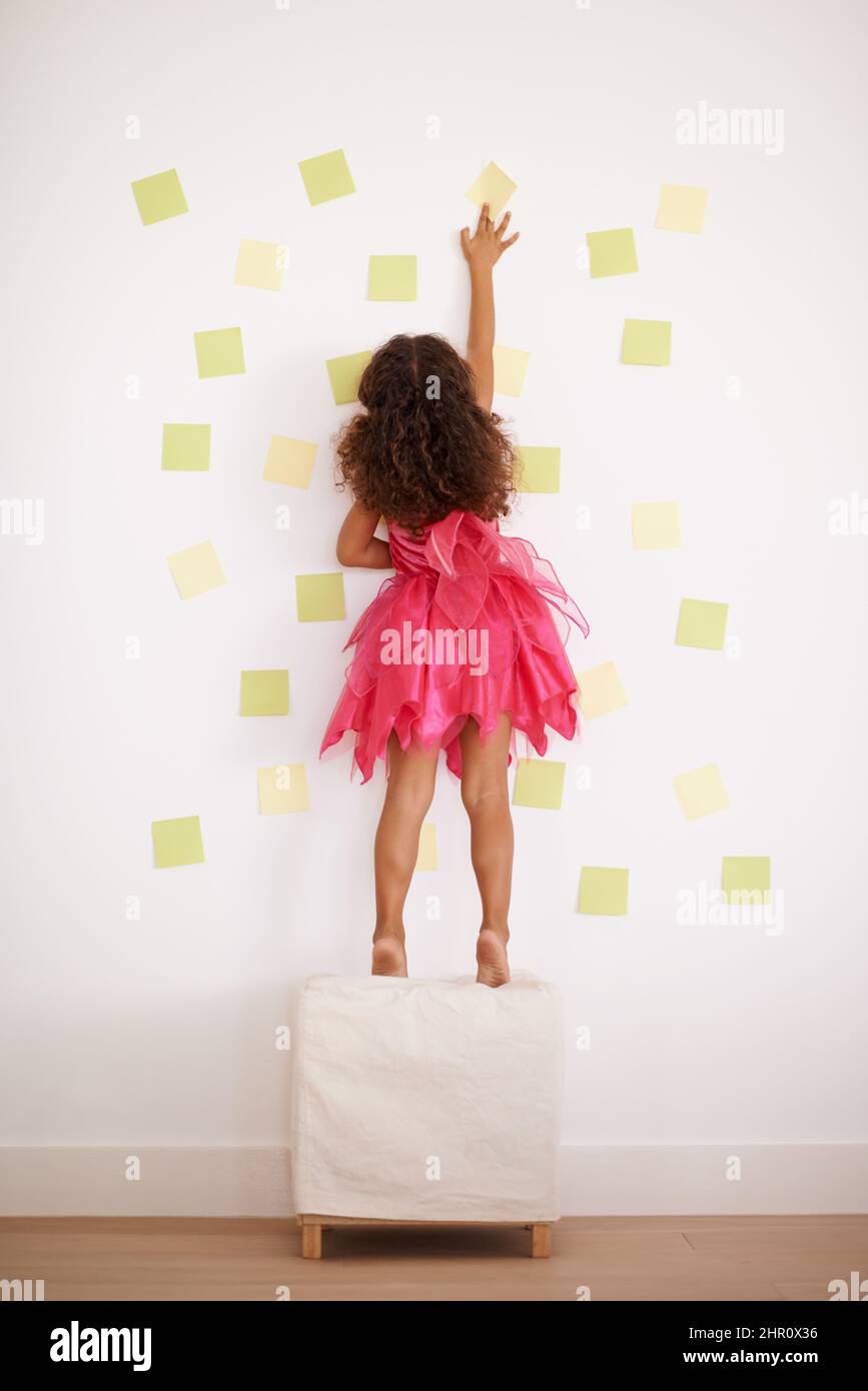 Giocare con il materiale appiccicoso. Vista posteriore di una bambina che attacca le note al muro. Foto Stock