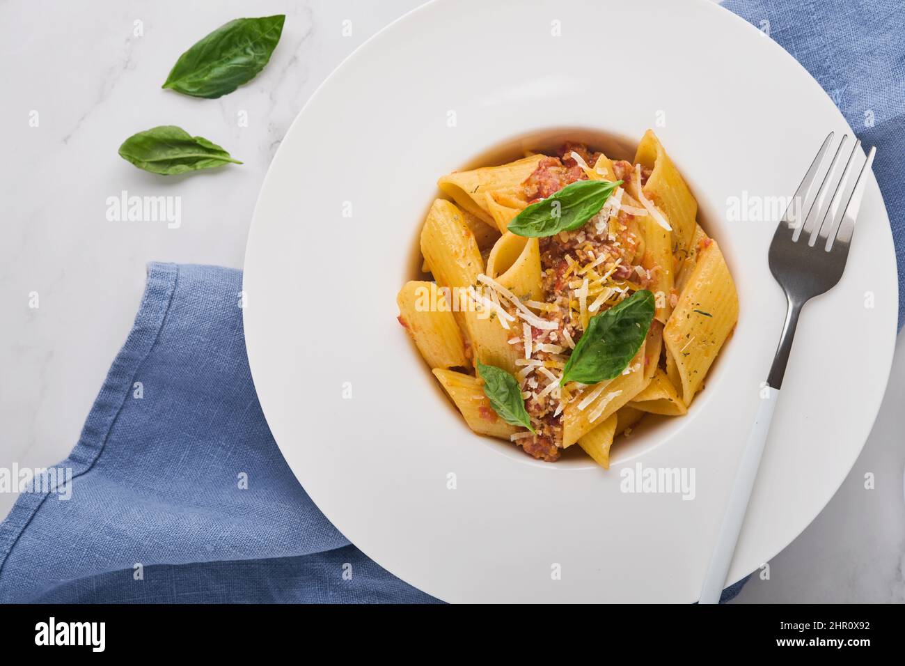 Penne alla bolognese. Gustosa e appetitosa pasta classica italiana a penne con parmigiano, basilico e salsa bolognese in piatto bianco su piastra di pietra Foto Stock