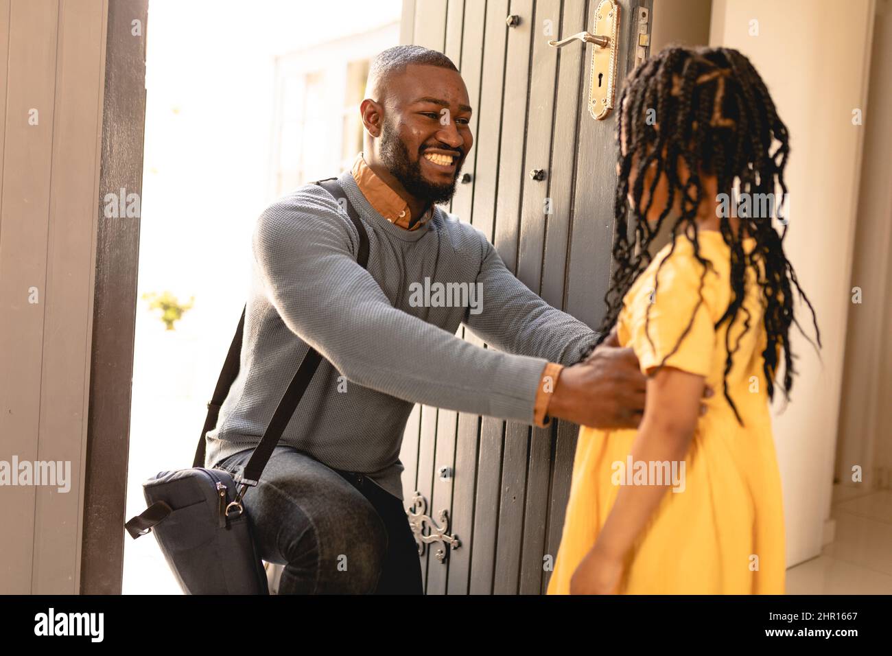Un uomo afro-americano felice si inginocchiò mentre salutò la figlia all'arrivo all'ingresso della casa Foto Stock