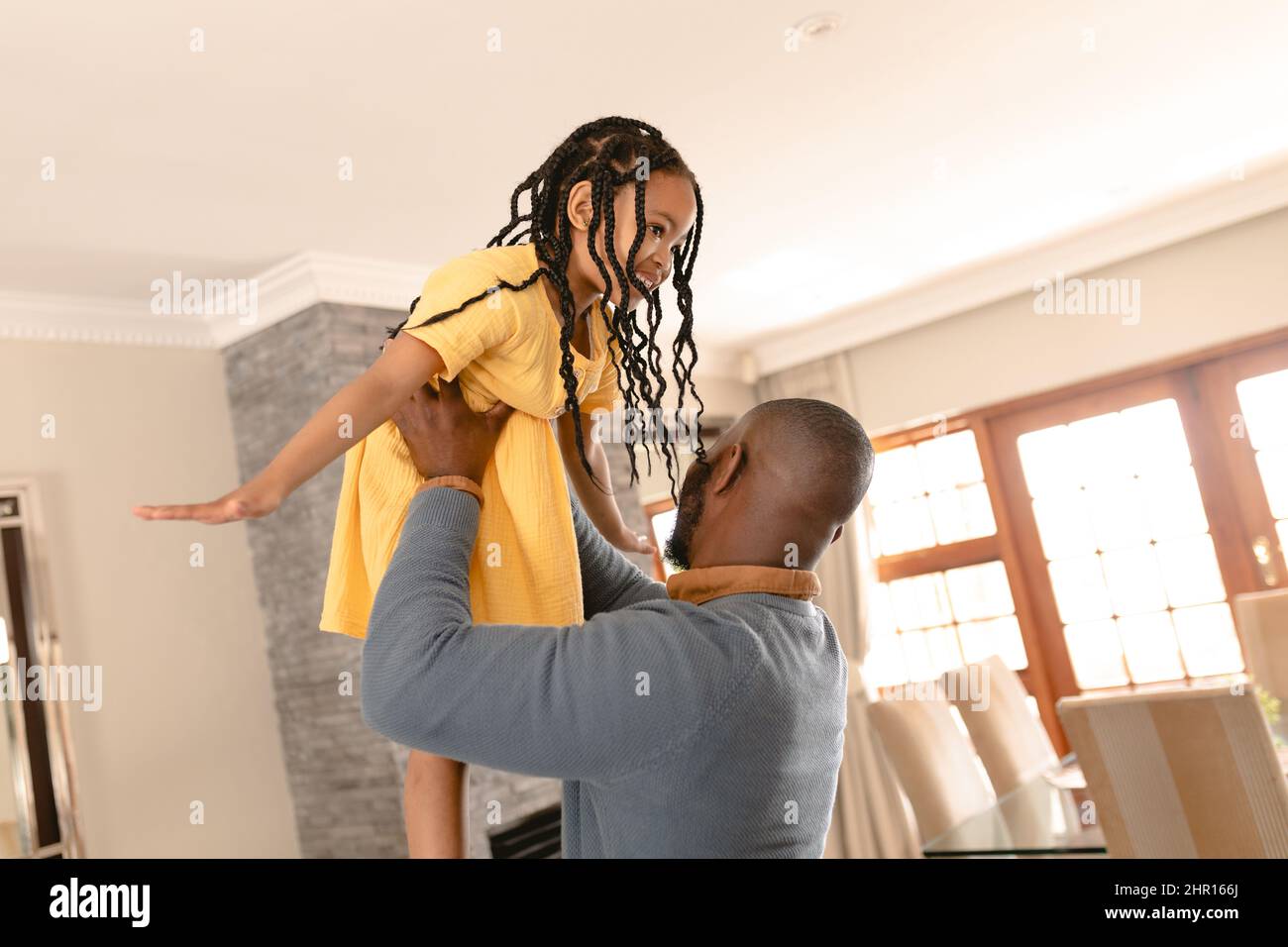 Felice ragazza afroamericana godendo di essere un aeroplano tenuto da padre in soggiorno a casa Foto Stock