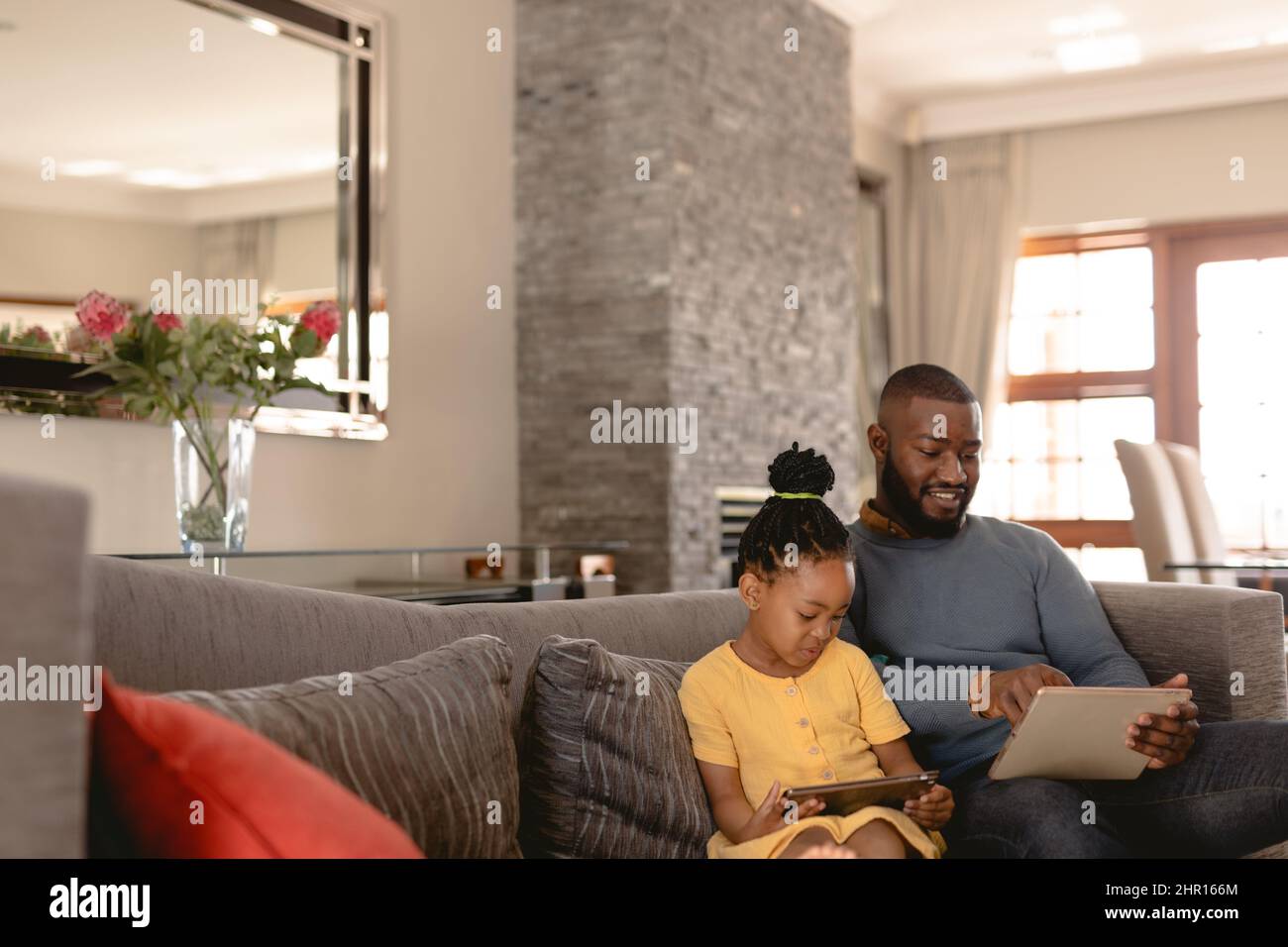 Felice uomo afroamericano che usa il tablet digitale dalla figlia mentre si siede insieme sul divano a casa Foto Stock