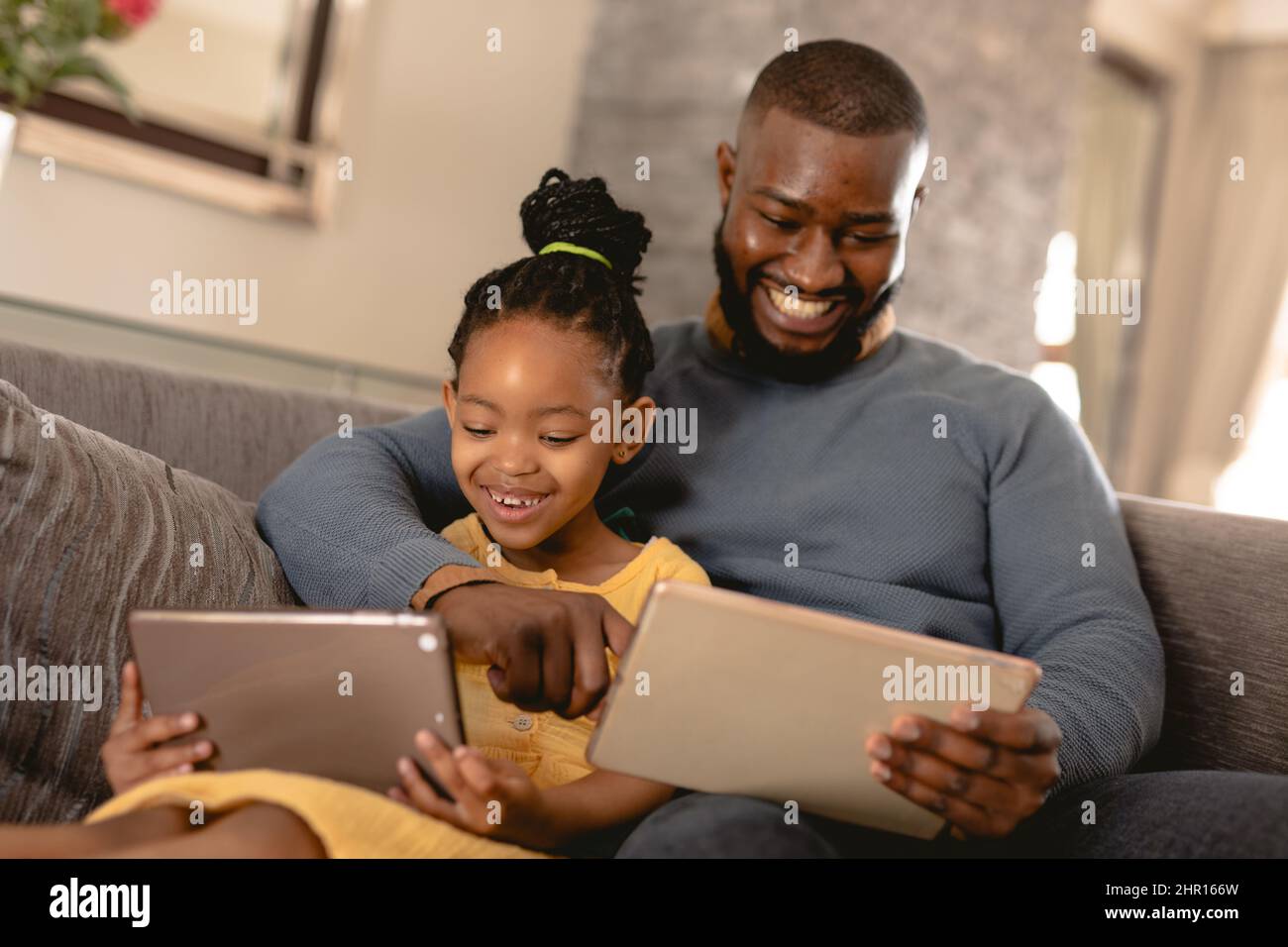 Felice padre e figlia afroamericana usando i PC digitali mentre si siede insieme sul divano a casa Foto Stock