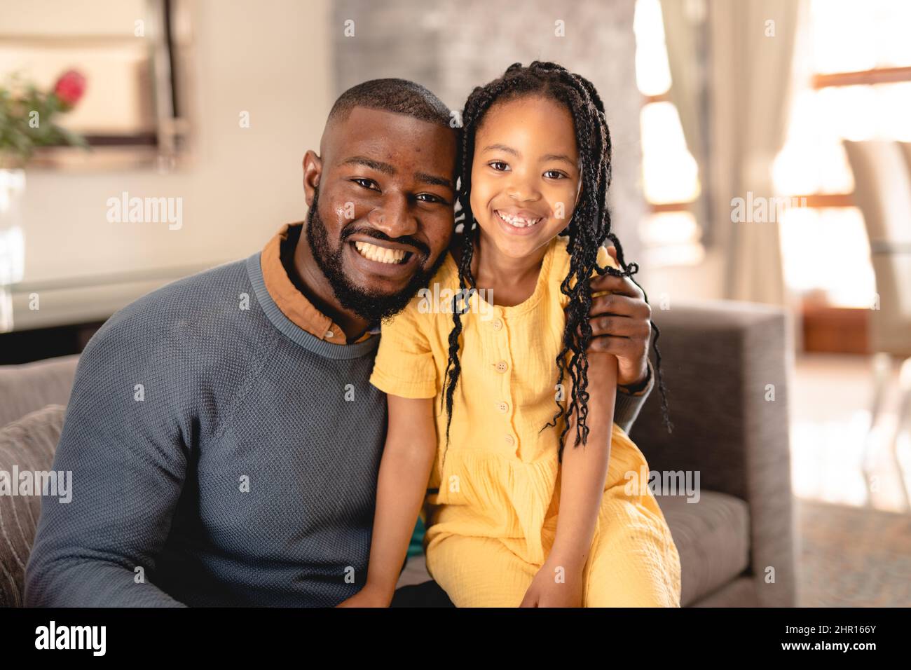 Ritratto di uomo afroamericano sorridente seduto con braccio intorno alla figlia sul divano in soggiorno Foto Stock