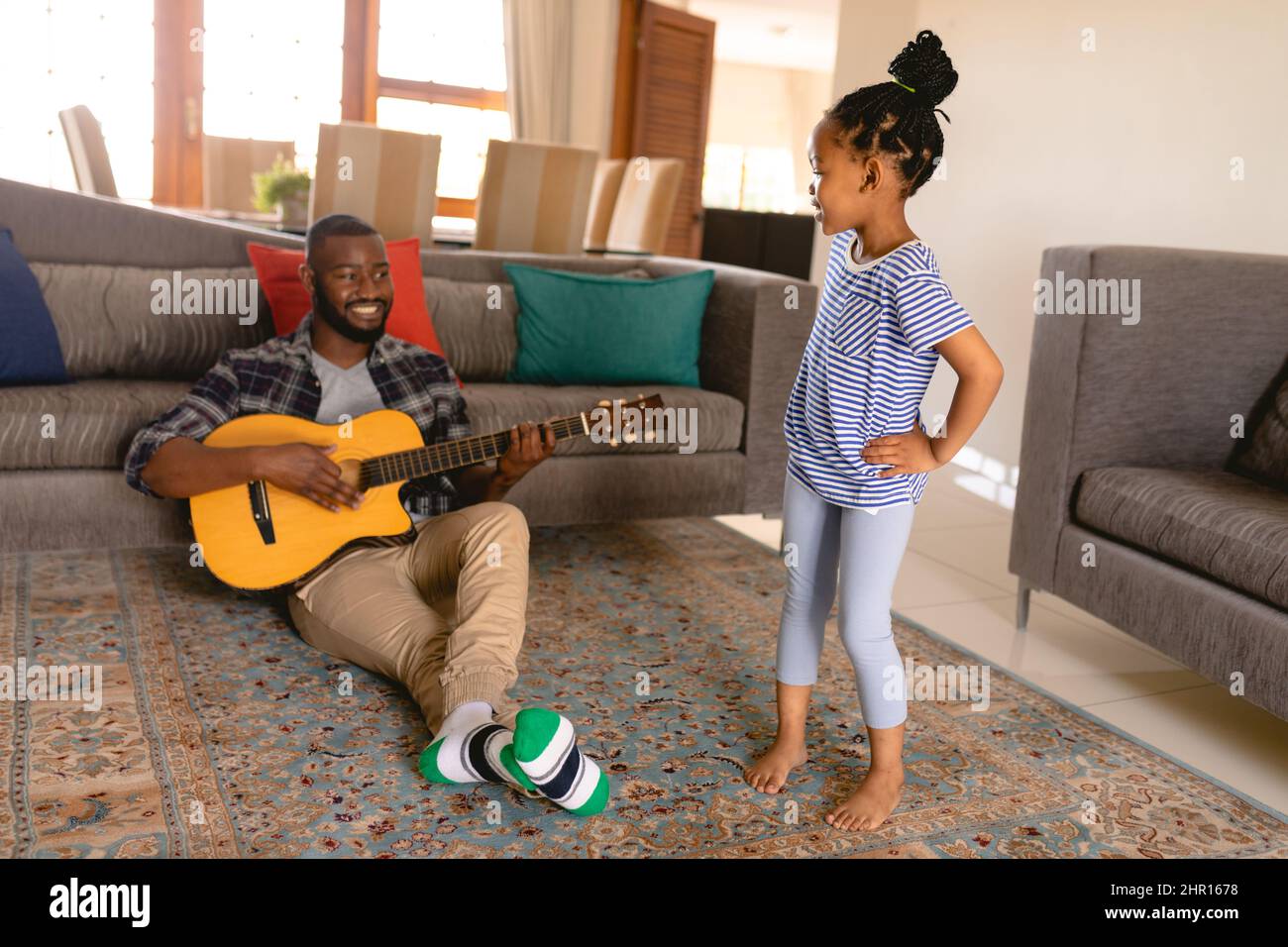 Carina ragazza afroamericana che balla davanti al padre mentre suona la chitarra mentre si siede a casa Foto Stock