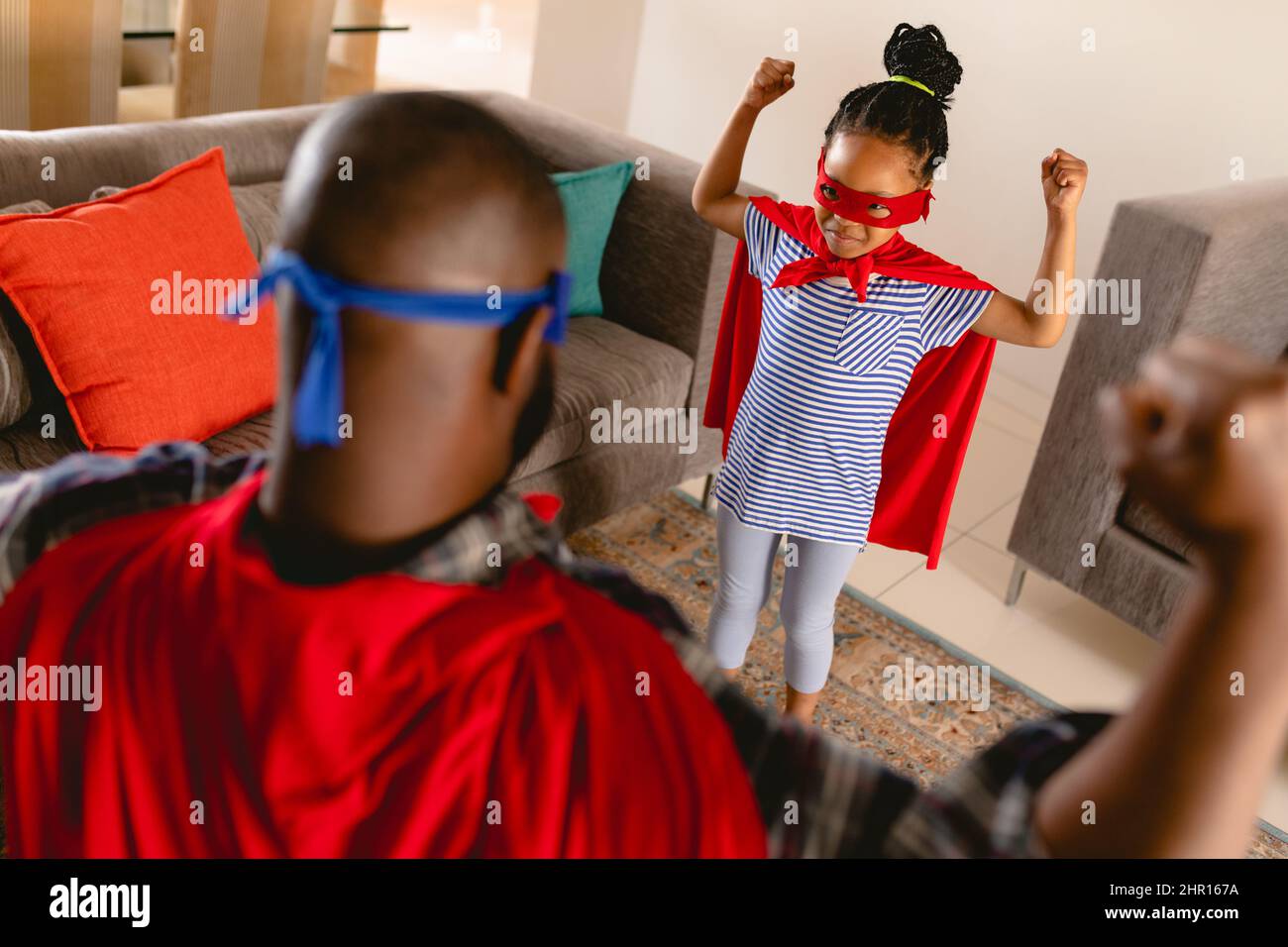 Giocoso afroamericano figlia e padre in costumi supereroi che flettono i muscoli Foto Stock