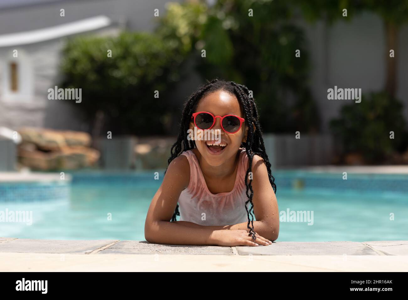 Ritratto della ragazza afro-americana felice carino indossando occhiali da sole appoggiati a bordo piscina il giorno di sole Foto Stock