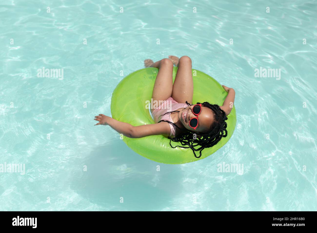 Vista ad alto angolo della ragazza afro-americana godendo giorno di sole seduto su anello gonfiabile in piscina Foto Stock