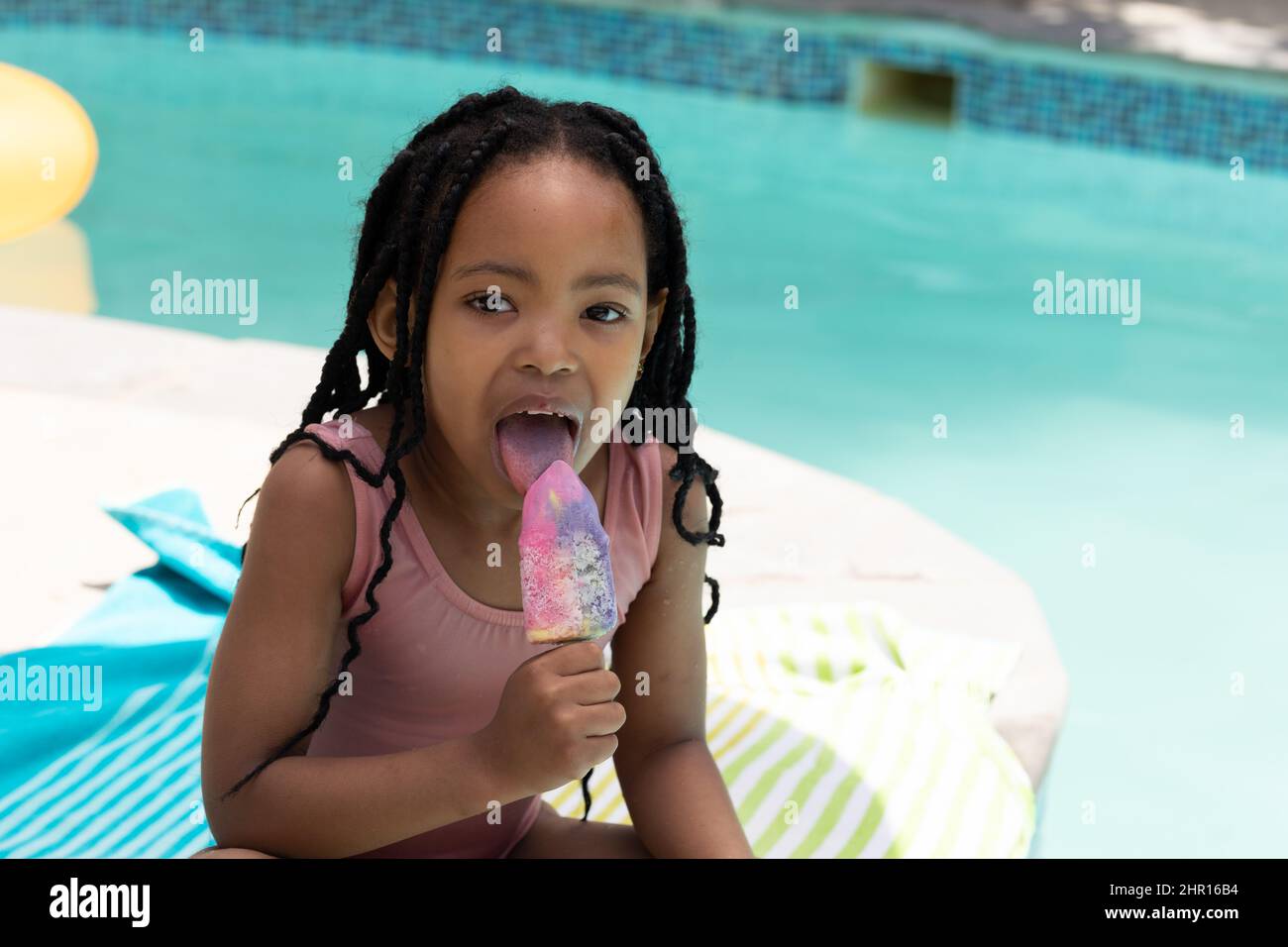 Ritratto di ragazza afroamericana carina mangiare gelato mentre si siede a bordo piscina in giorno di sole Foto Stock