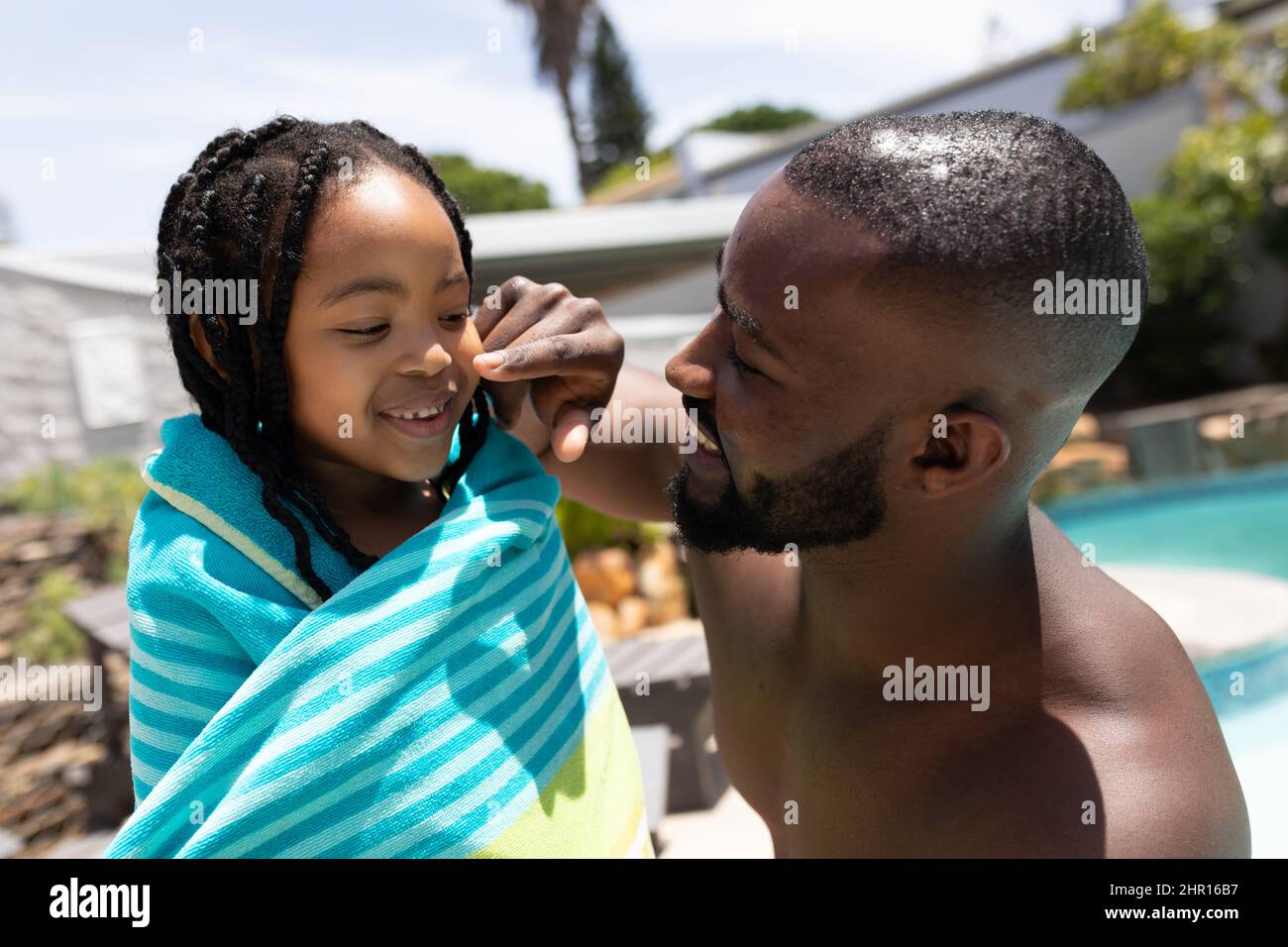 Felice padre afroamericano che tocca il naso della figlia a bordo piscina il giorno di sole Foto Stock