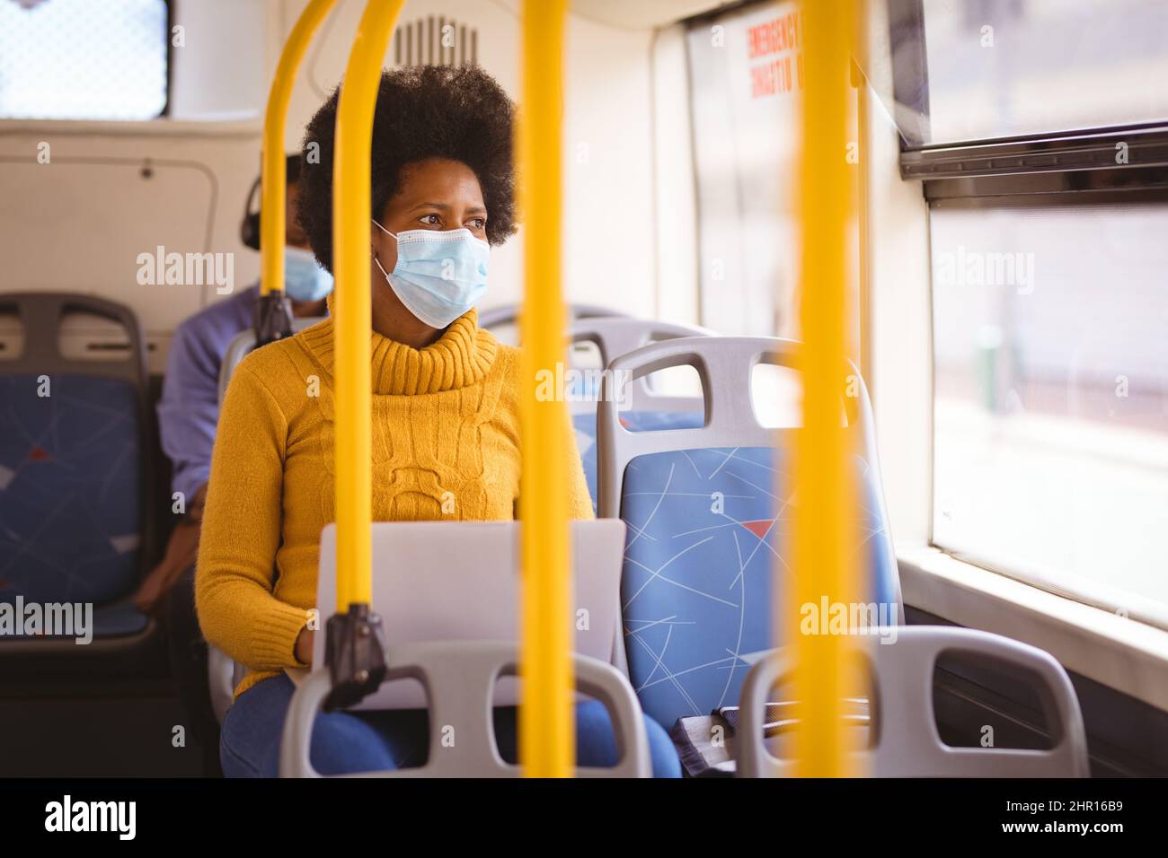 Donna d'affari afroamericana di metà adulto che indossa la maschera guardando via mentre si siede con il portatile in autobus Foto Stock