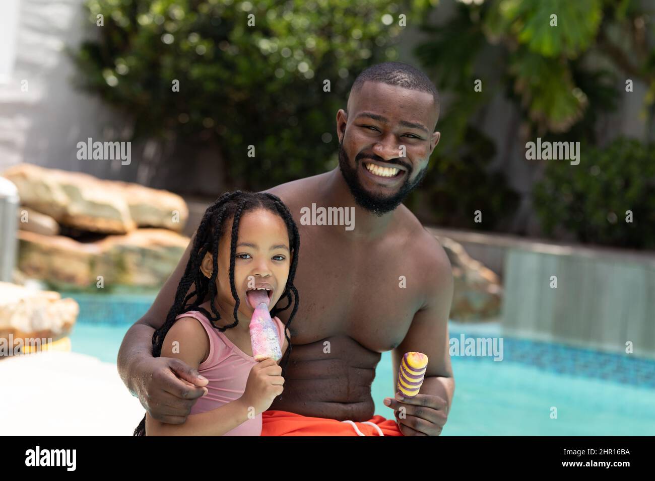 Ritratto di padre e figlia afro-americana felice mangiare gelato e papà a bordo piscina Foto Stock