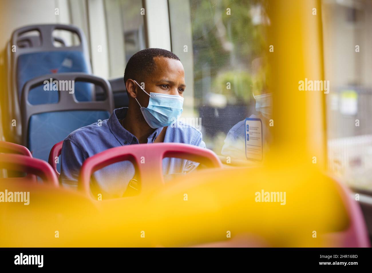 Uomo d'affari africano americano medio adulto che indossa maschera guardando lontano mentre si viaggia in autobus Foto Stock