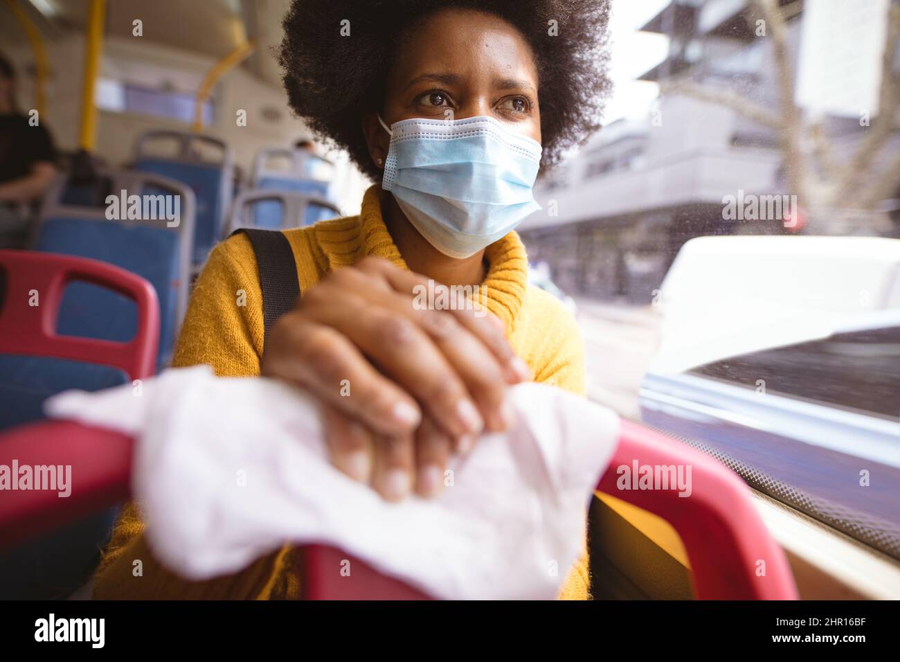 Donna d'affari afroamericana di metà adulto con maschera che tiene il sedile con tovagliolo mentre viaggia in autobus Foto Stock