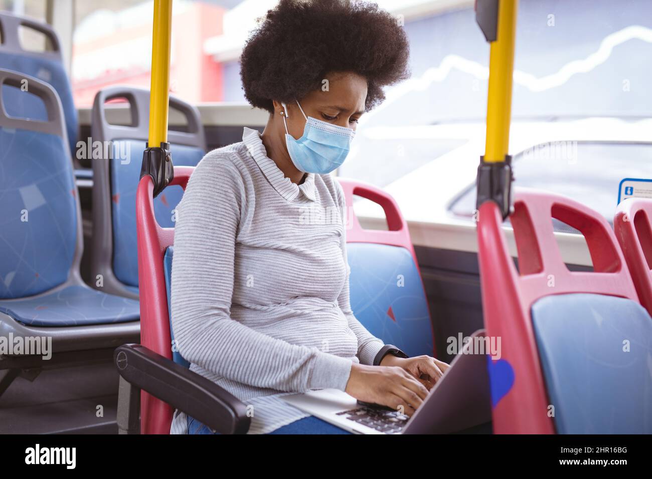 Donna d'affari afroamericana di metà adulto con maschera usando il laptop mentre viaggia in autobus Foto Stock