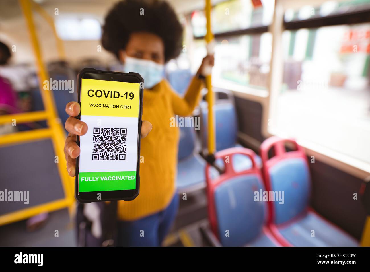 Donna d'affari afroamericana di metà adulto che mostra il telefono con codice di qr completamente vaccinato del codice di covid-19 in bus Foto Stock