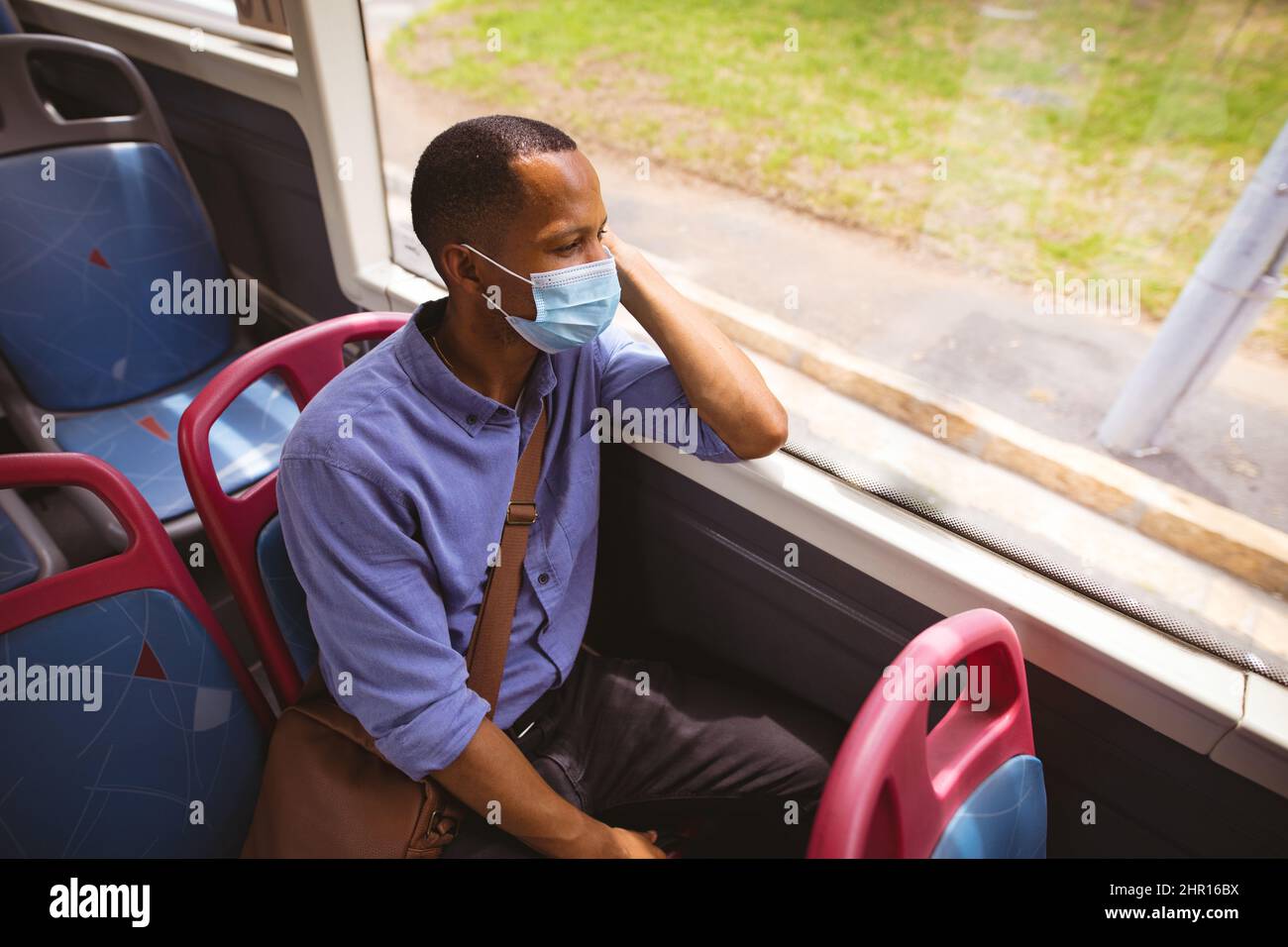 Uomo d'affari africano americano medio adulto che indossa maschera mentre si siede con borsa a spalla in autobus Foto Stock