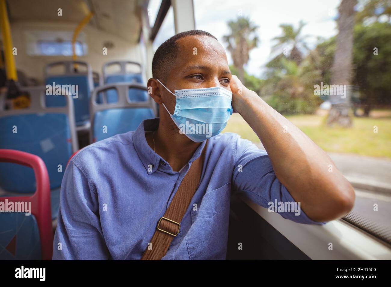 African american uomo d'affari adulto medio indossare maschera guardando lontano mentre si siede alla finestra sedile in autobus Foto Stock