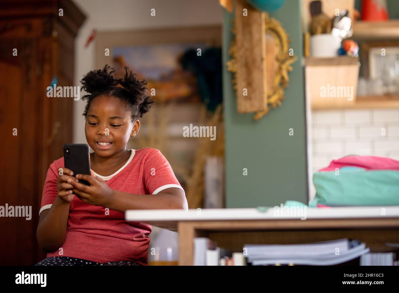 Sorridendo ragazza afroamericana usando lo smart phone mentre si siede al tavolo Foto Stock