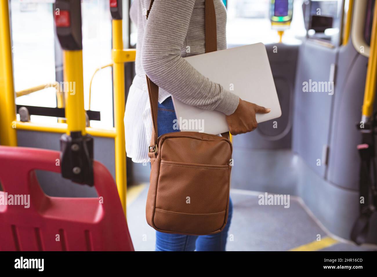 Parte centrale della donna d'affari afroamericana con borsa a spalla e laptop in piedi in autobus Foto Stock